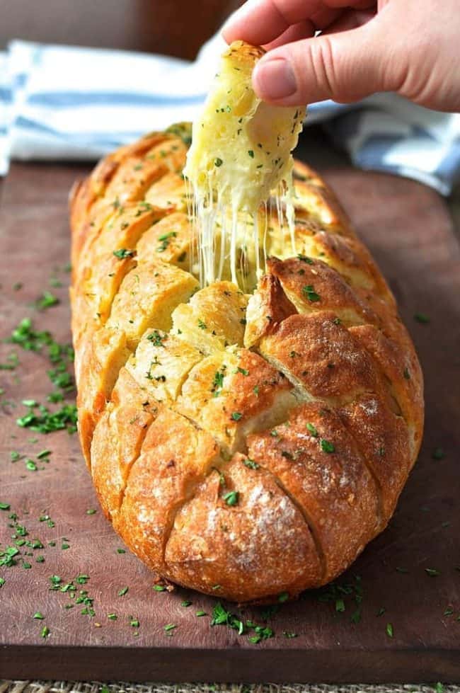 A loaf of cheese and garlic crackbread with a piece being pulled out.