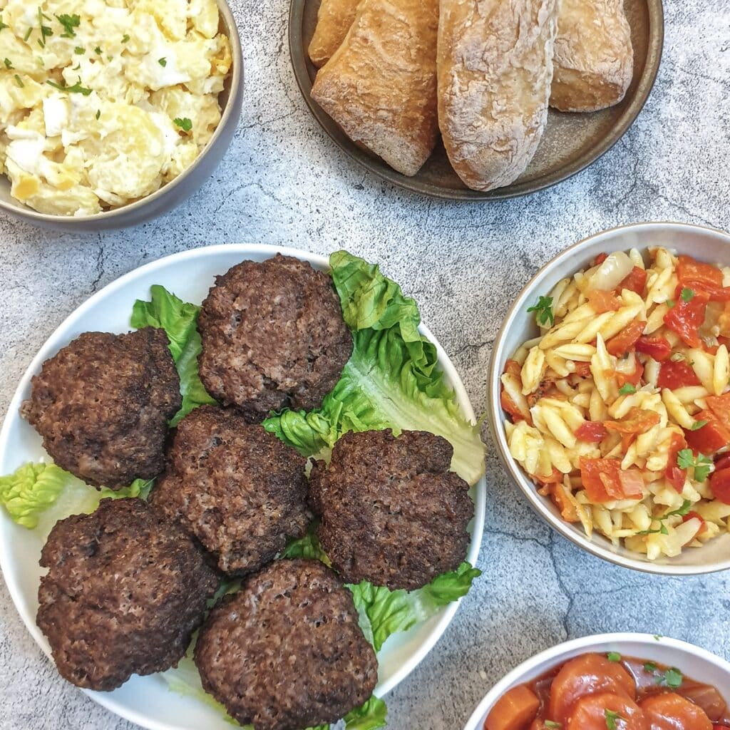 6 boerewors patties on a plate surrounded by bowls of salads.