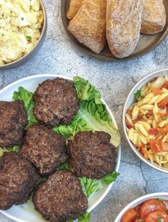 6 boerewors patties on a plate surrounded by bowls of salads.