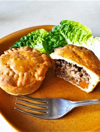 Two mini beef and onion pies on a plate with lettuce.