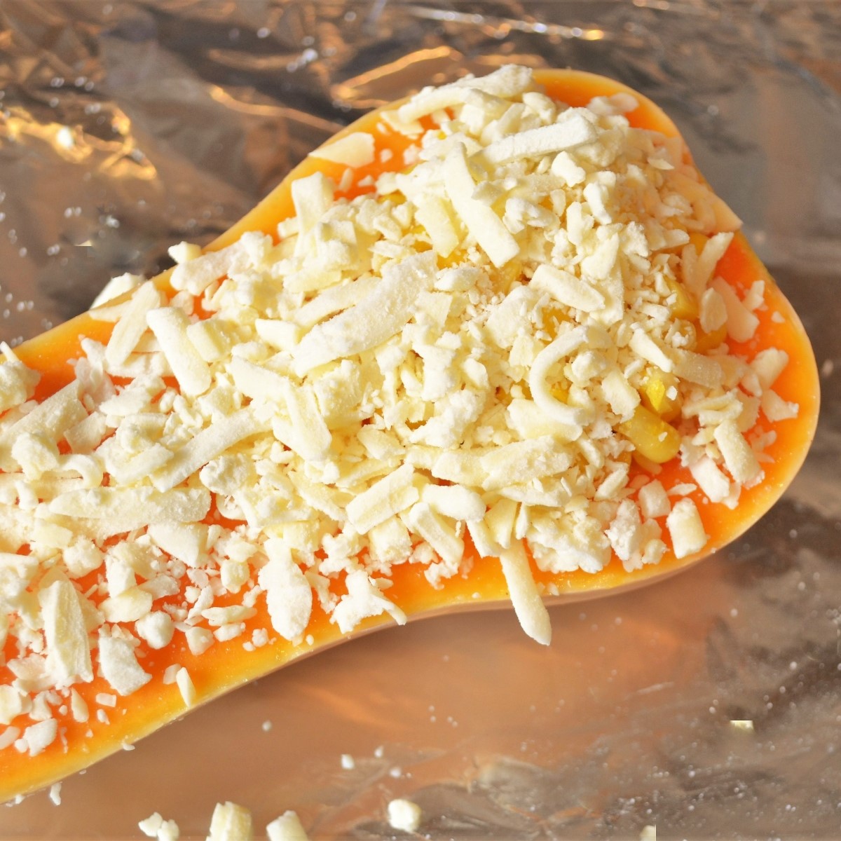 Half a butternut, stuffed with cheese and corn, on a baking tray.