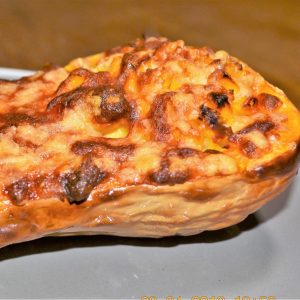 Half a baked butternut, stuffed with cheese and corn, on a plate.