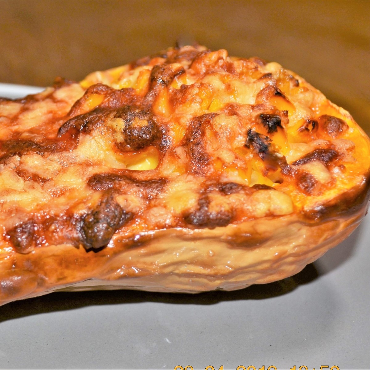 Half a baked butternut, stuffed with cheese and corn, on a plate.
