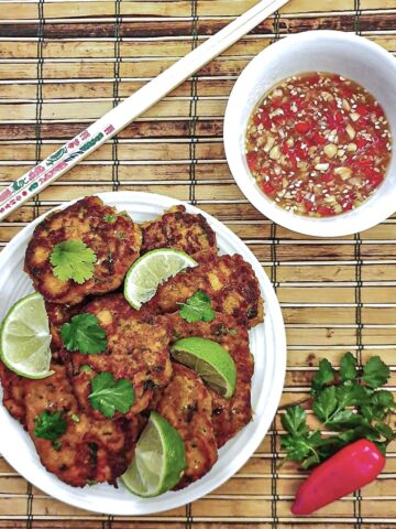 A plate of Thai salmon fishcakes next to a bowl of spicy dipping sauce.