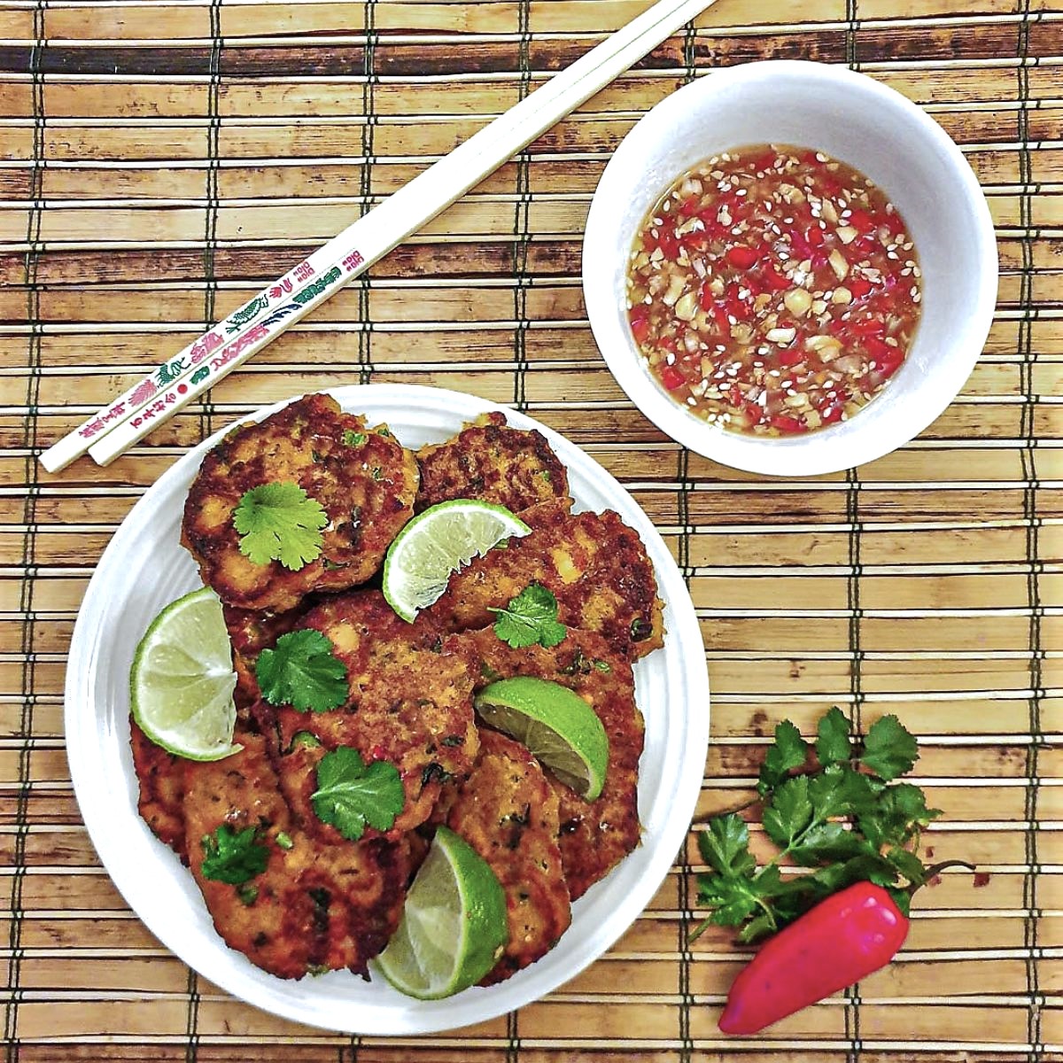A plate of Thai salmon fishcakes next to a bowl of spicy dipping sauce.
