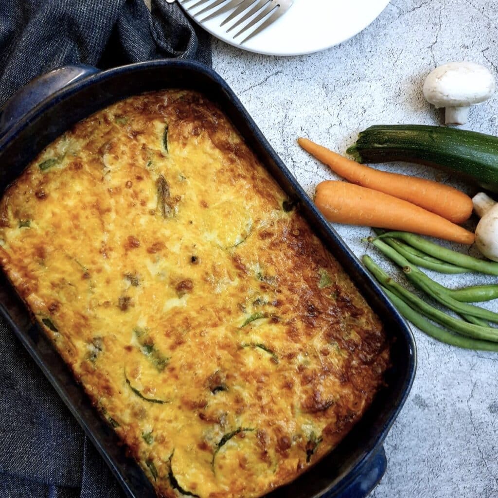 Overhead shot of a crustless vegetable quiche next to a pile of fresh vegetables.