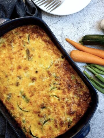 Overhead shot of a crustless vegetable quiche next to a pile of fresh vegetables.