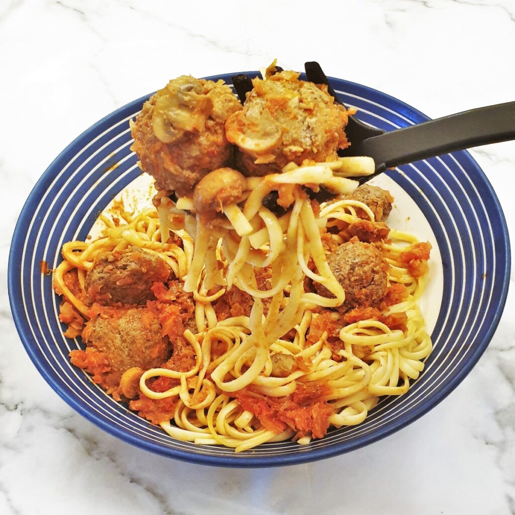 A spoonful of spaghetti and meatballs being lifted from the dish.