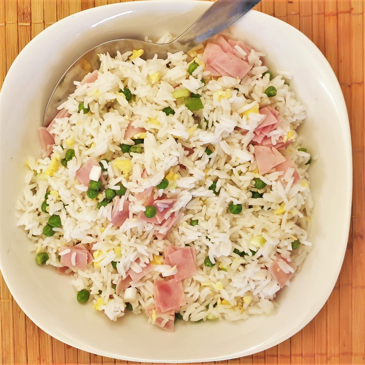 Overhead shot of a serving bowl filled with egg fried rice with egg, chopped ham and peas