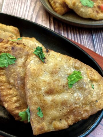 Crispy cheese and sweetcorn samosas on a black plate.