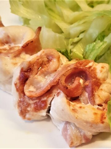 Close up of a chicken and bacon skewer, with a pile of lettuce on the side.