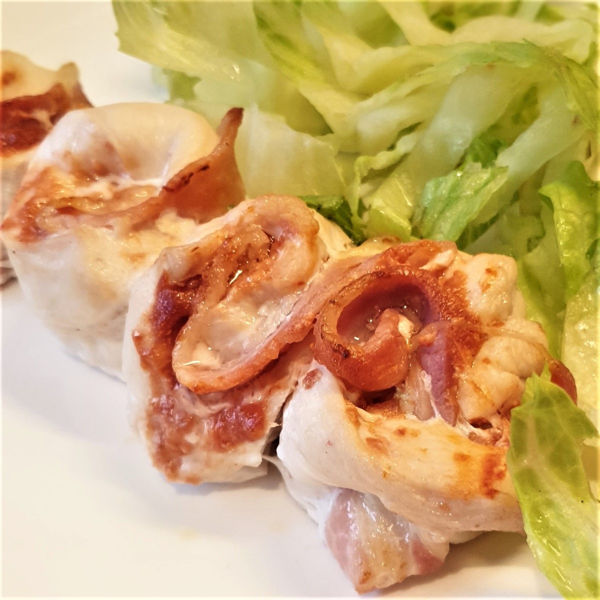 Close up of a chicken and bacon skewer, with a pile of lettuce on the side.