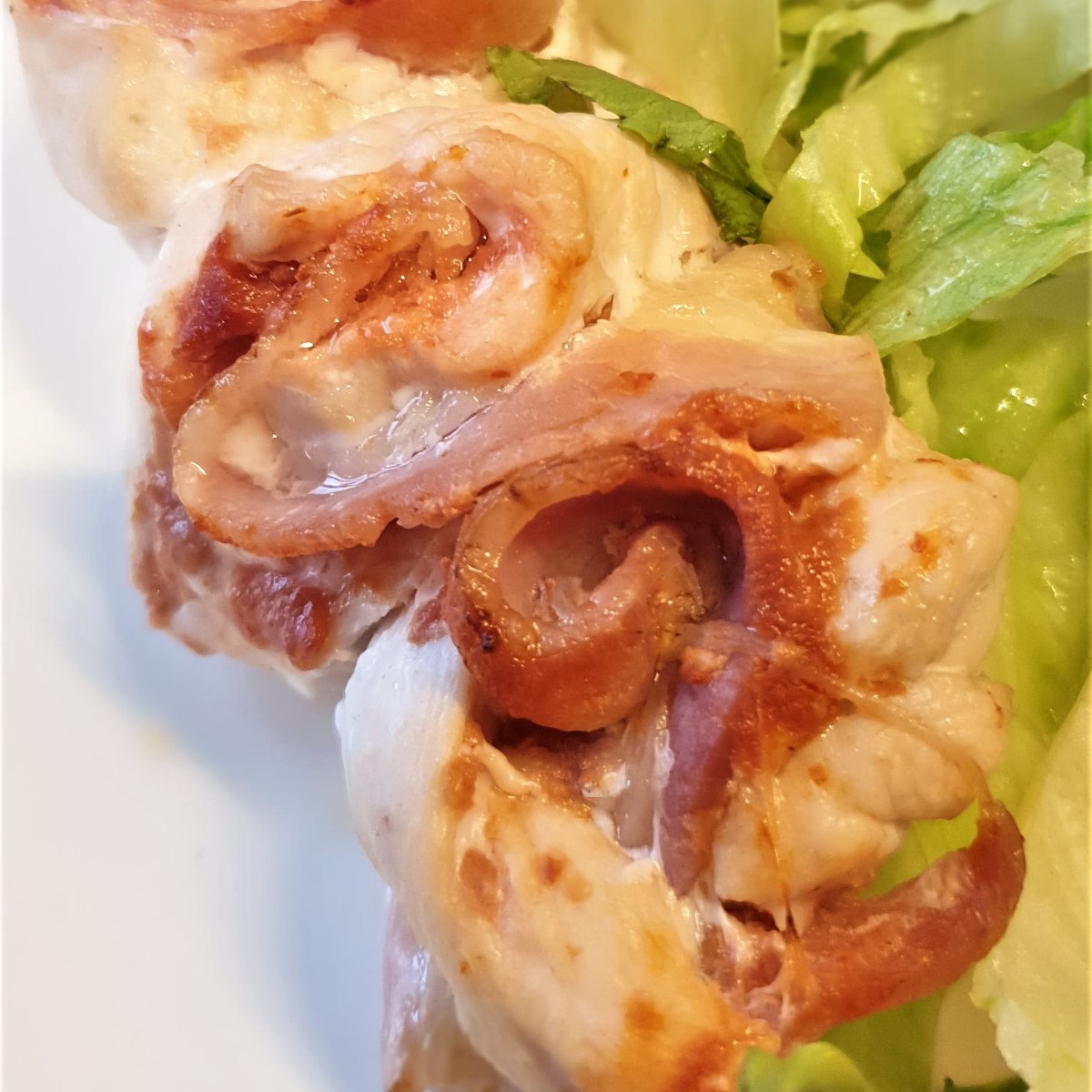 Close up of a chicken and bacon skewer, with a pile of lettuce on the side.