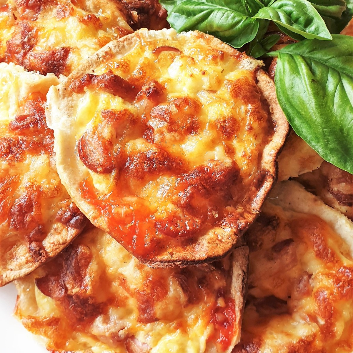 Eggy cheesy things are delicious morsels of egg, sausage and cheese baked on rounds of fajita wraps. Perfect for nibbling while waiting for barbeque to be ready. Give them a try at your next get-together - I'm sure you'll love them. #barbeque #partysnacks #miniquiche Close up of an eggy cheese thing.
