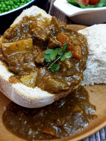 A hollowed-out loaf of bread on a plate, filled with beef curry.