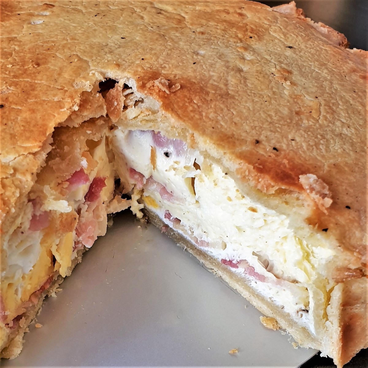 A bacon and egg pie with a slice removed to show the inside.