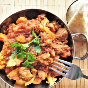 A bowl of lamb curry alongside a dish of naan bread.