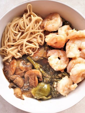 A bowl of honey garlic shrimp with saucy steamed vegetables and noodles.