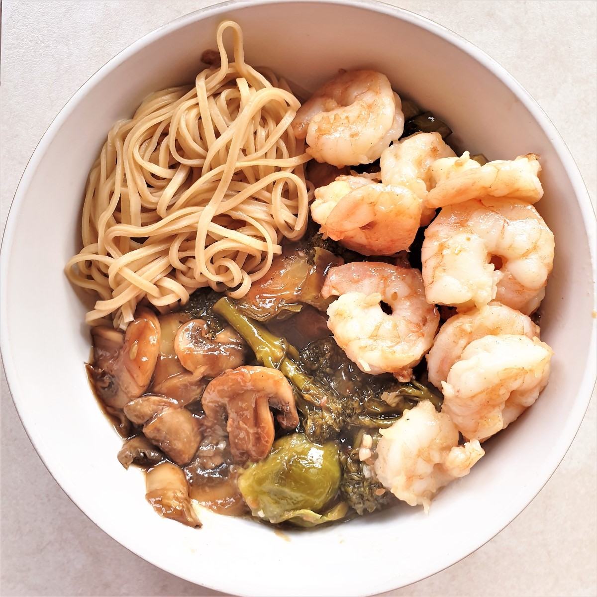 A bowl of honey garlic shrimp with saucy steamed vegetables and noodles.