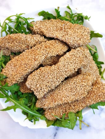 A pile of sesame-coated chicken strips on a bed of rocket.