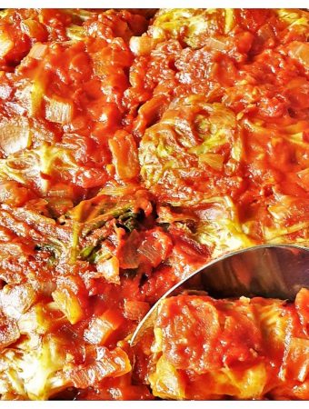 A dish of baked stuffed cabbage rolls with a spoon.