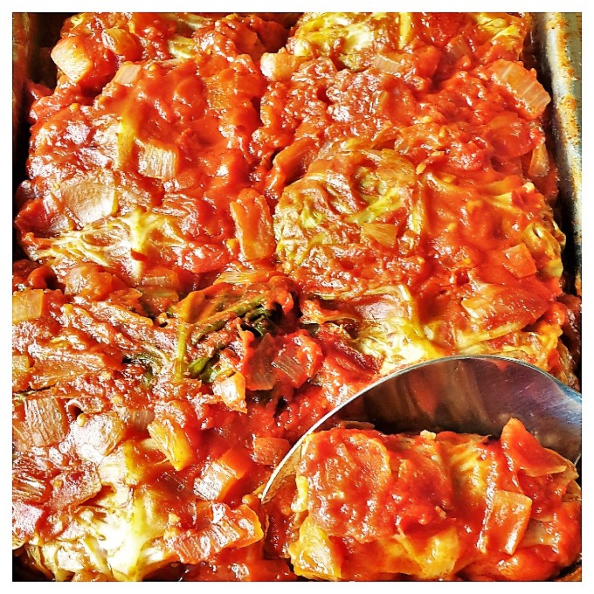A dish of baked stuffed cabbage rolls with a spoon.