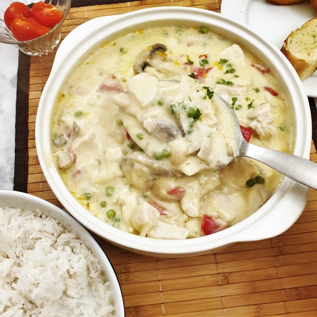 This easy Chicken a la King recipe is made from tender chicken chunks, red peppers and mushrooms in a creamy sauce. It's on the table in 30 minutes - start to finish. Perfect for those days when you don't have much time to spend in the kitchen. #chickenalaking #classicmeals #chicken #easysuppers #foodleclub Chicken a la king being spooned from a serving dish.