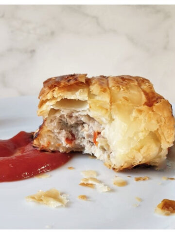 A pork and apple sausage roll on a plate with tomato ketchup.