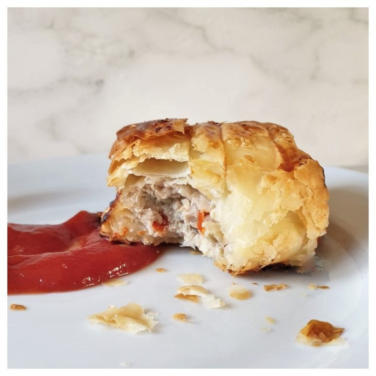 A pork and apple sausage roll on a plate with tomato ketchup.