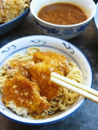 Pieces of crispy chicken covered in orange sauce, in a bowl with chopsticks.