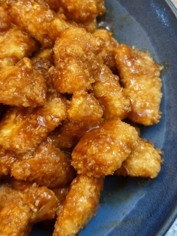 A blue serving dish filled with pieces of sticky orange chicken.