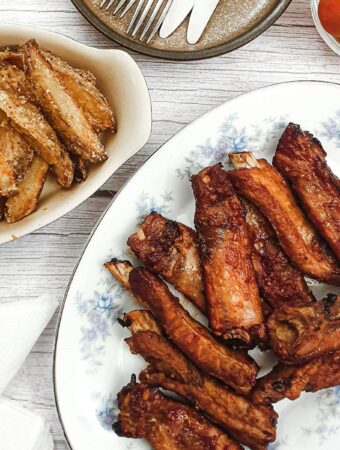 Sticky pork ribs on plate next to a dish of potato wedges.