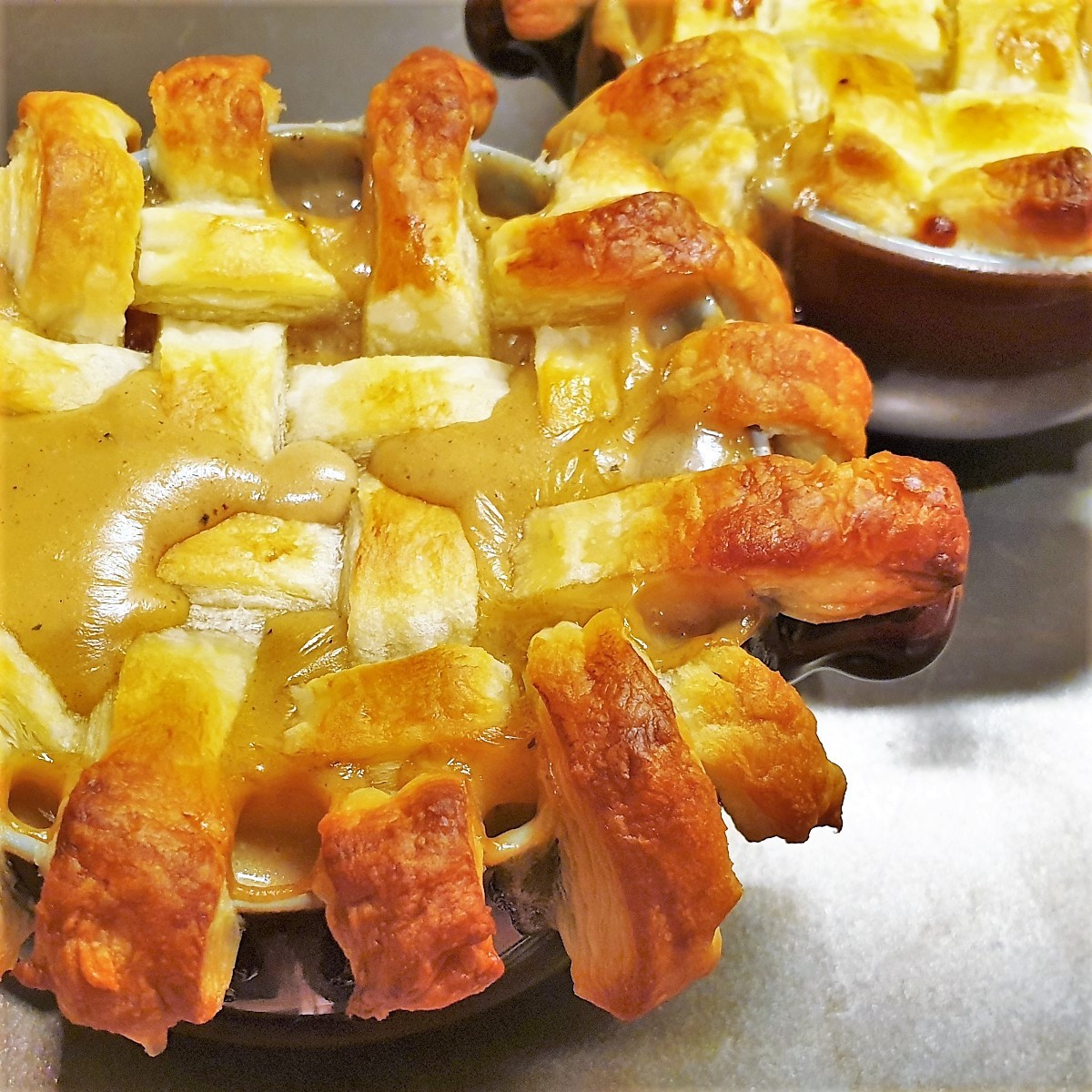 A beef pot pie topped with a lattice of puff pastry showing the gravy soaking through.