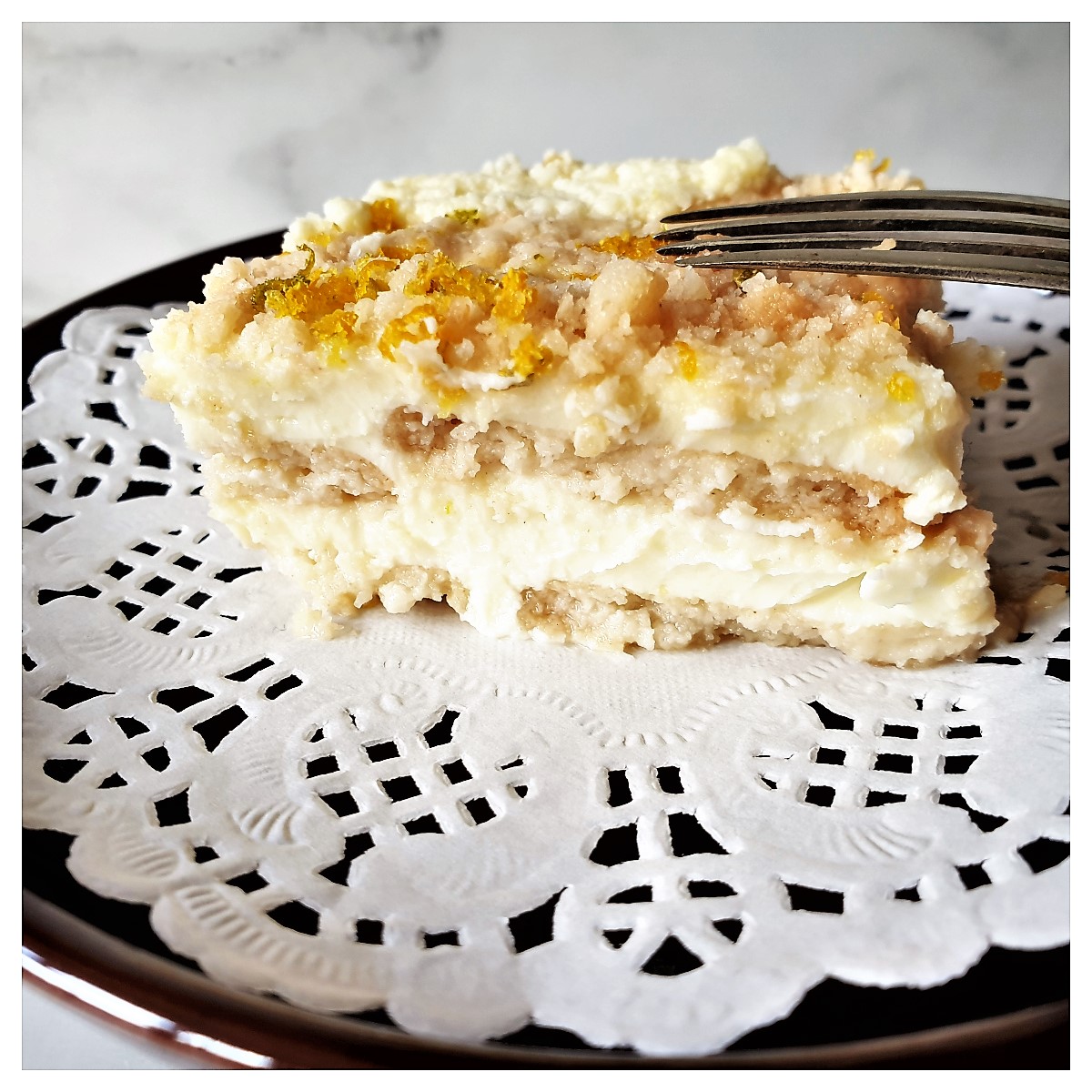 A slice of citrus cheesecake on on a doily on a brown plate.