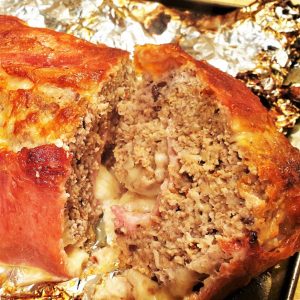 A cooked bacon covered meatloaf on tinfoil.