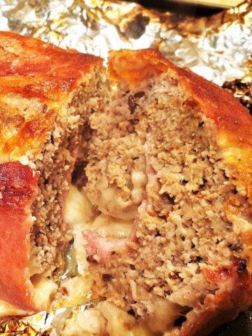 A cooked bacon covered meatloaf on tinfoil.