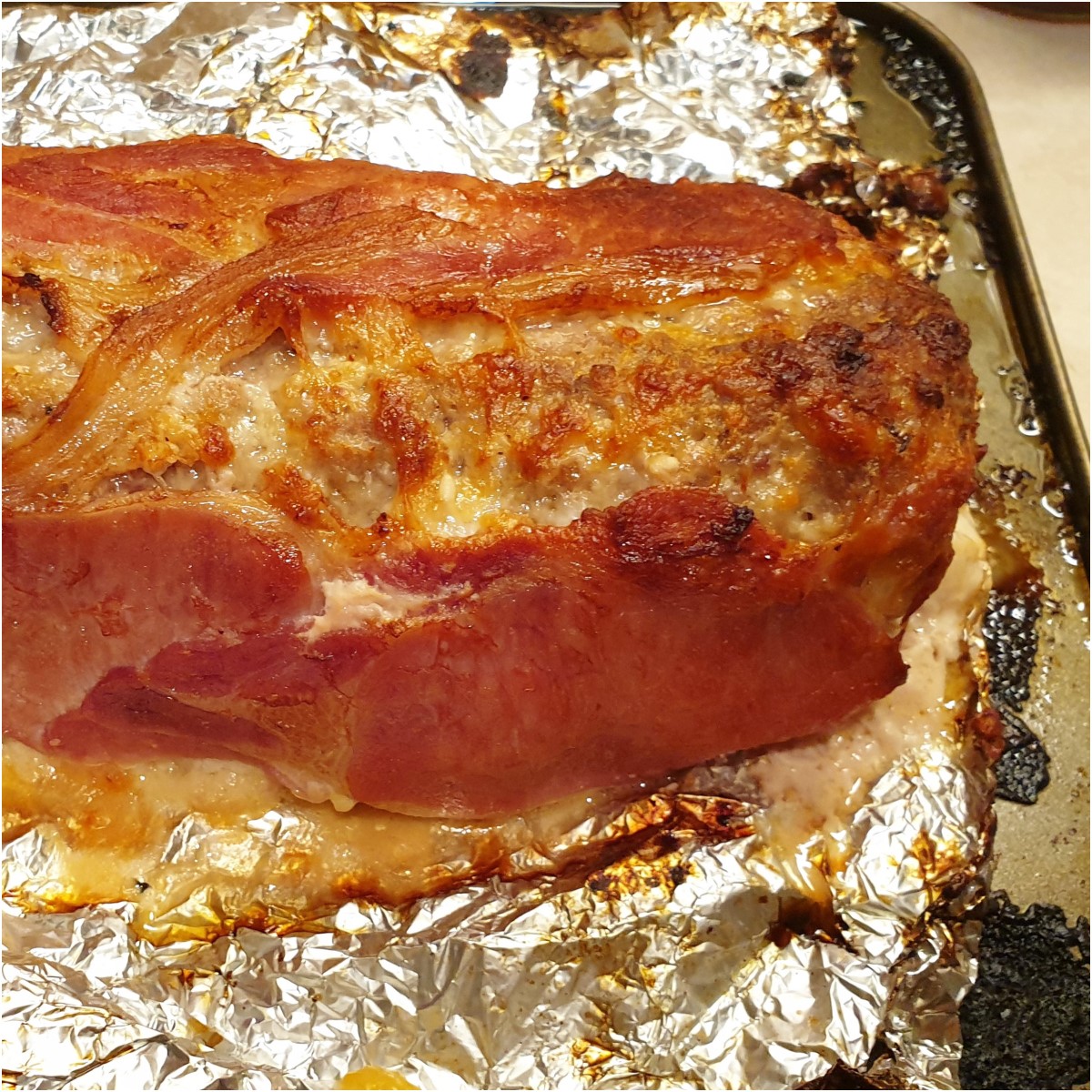 A cooked bacon covered meatloaf on tinfoil.