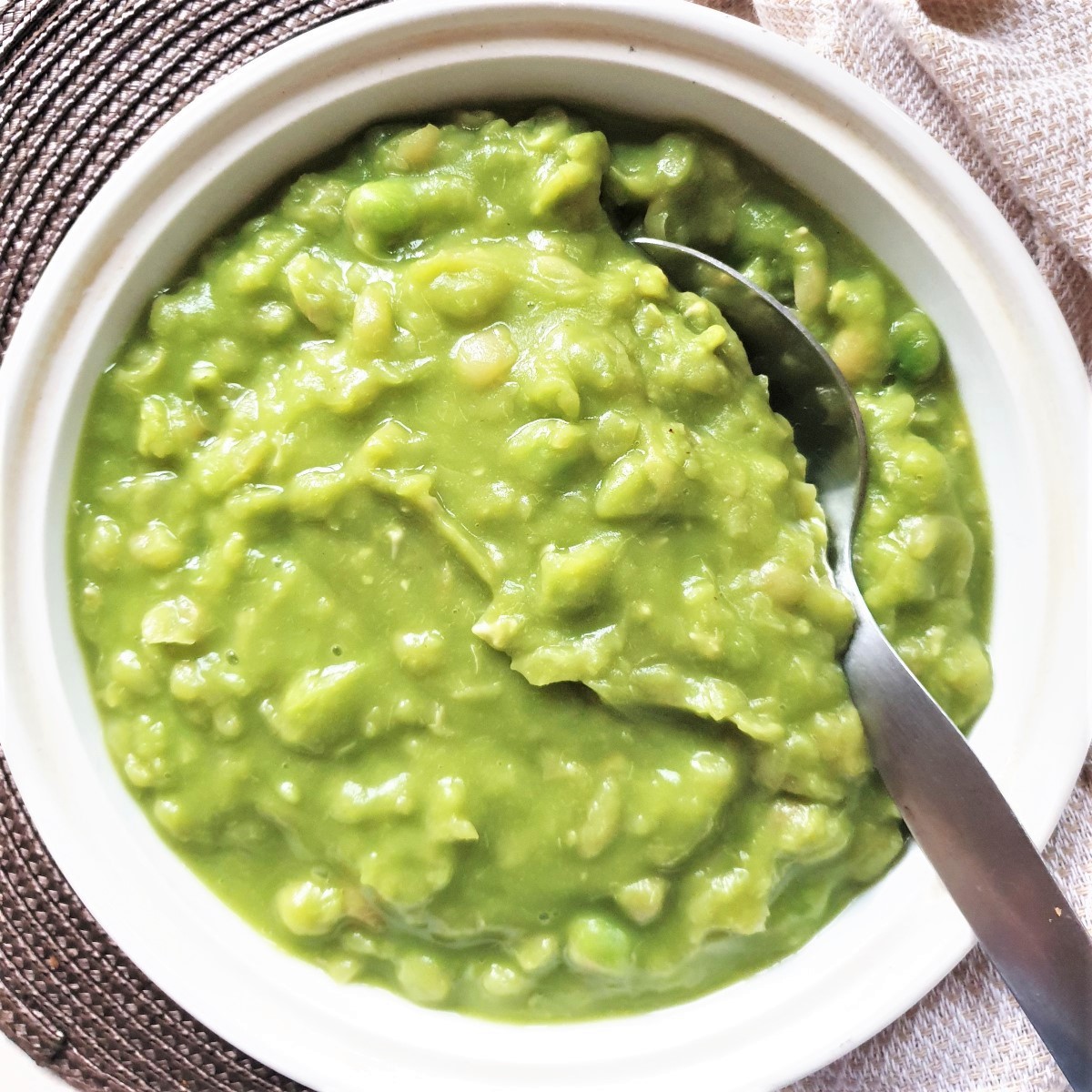 A large bowl of mushy peas with a spoon.