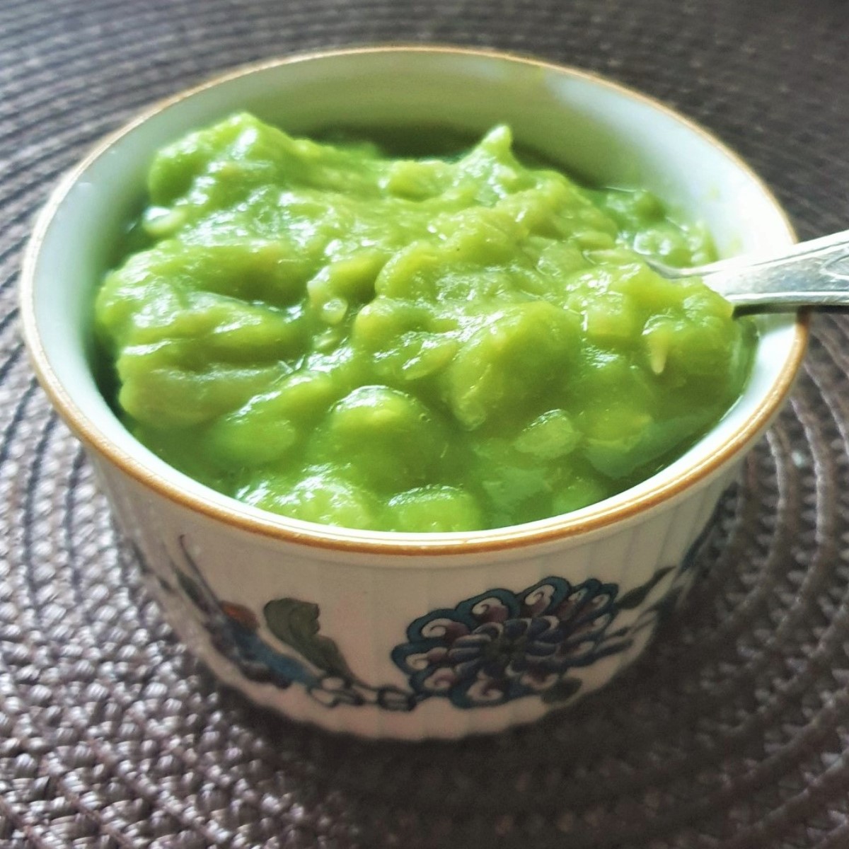 A small bowl of mushy peas with a spoon.