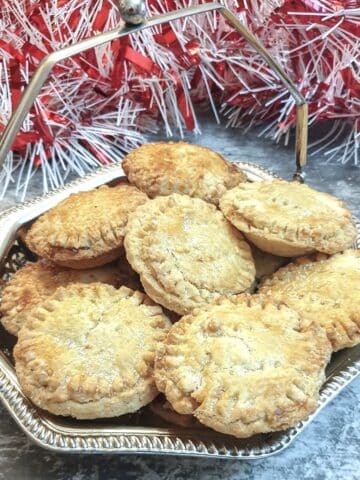 A silver dish of Christmas mince pies in front of a pile of red and white tinsel.