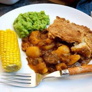 A helping of meat and potato pie on a plate with vegetables.