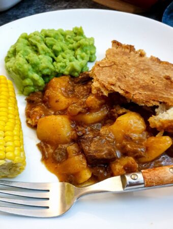 A helping of meat and potato pie on a plate with vegetables.