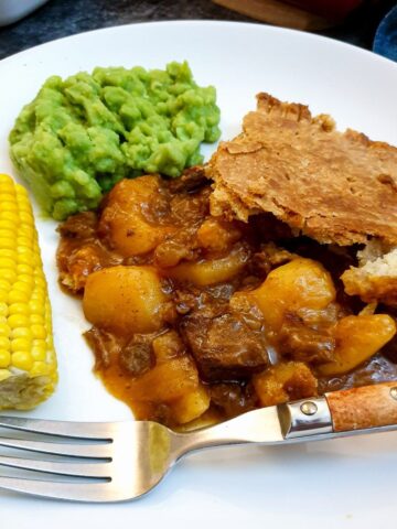 A helping of meat and potato pie on a plate with vegetables.