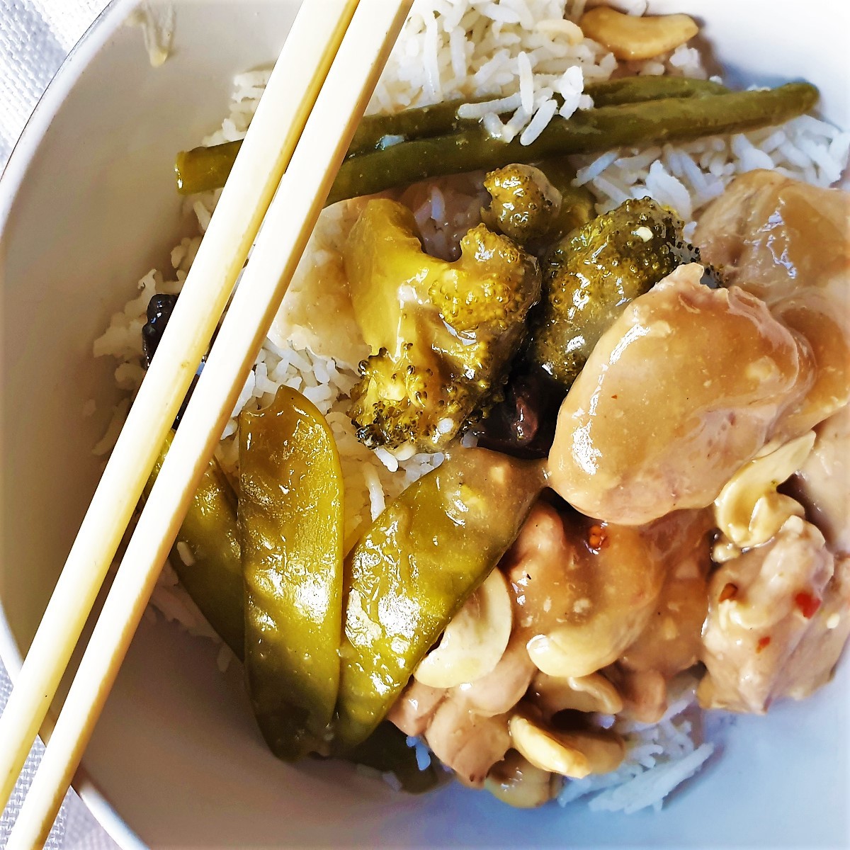 A dish of cashew nut chicken in a bowl with chopsticks.