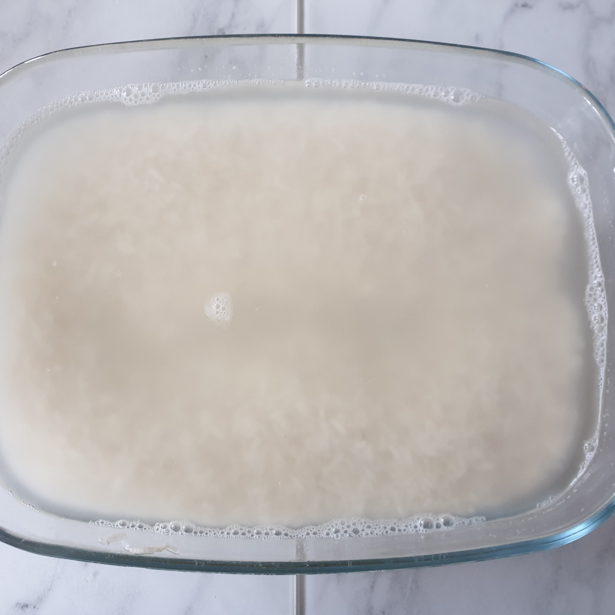 A baking dish containing rice covered in water.