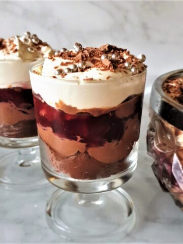 2 individual trifles next to a larger bowl of trifle.