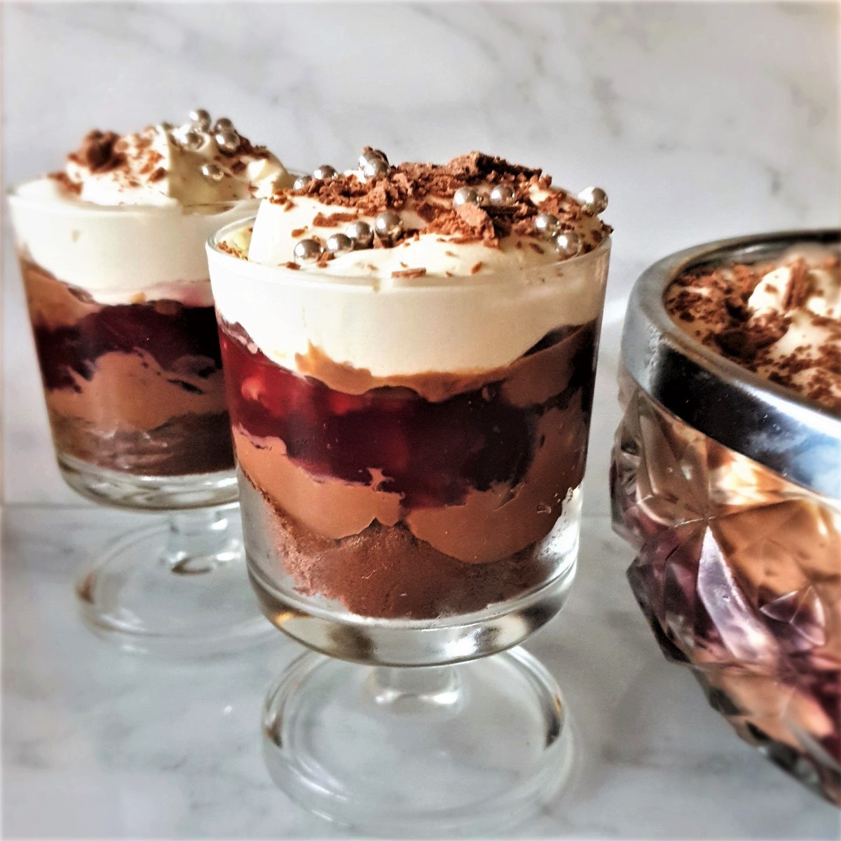 2 individual trifles next to a larger bowl of trifle.