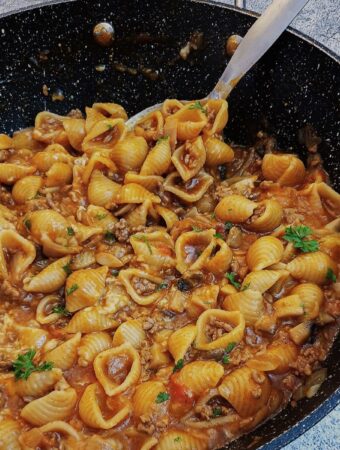 Cheesy mince pasta in a large pan with a spoon.