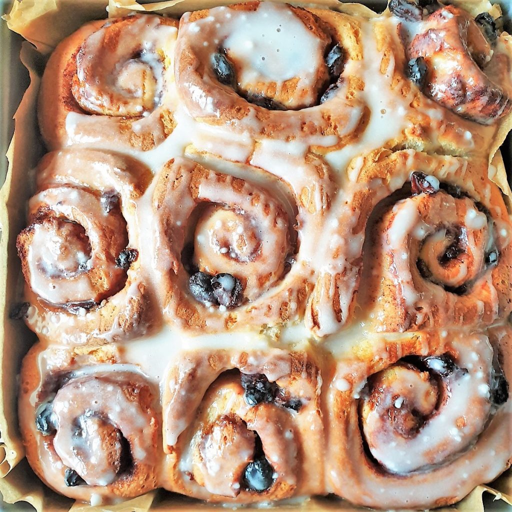 A tray of baked chelsea buns covered with glaze.