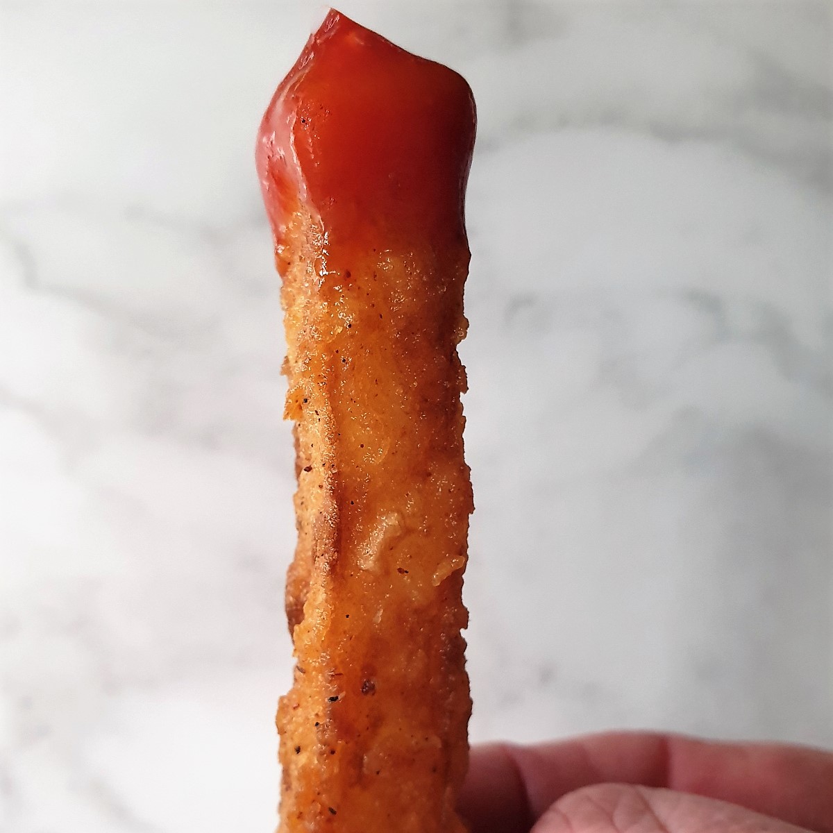 A crispy potato fry dipped in tomato sauce.